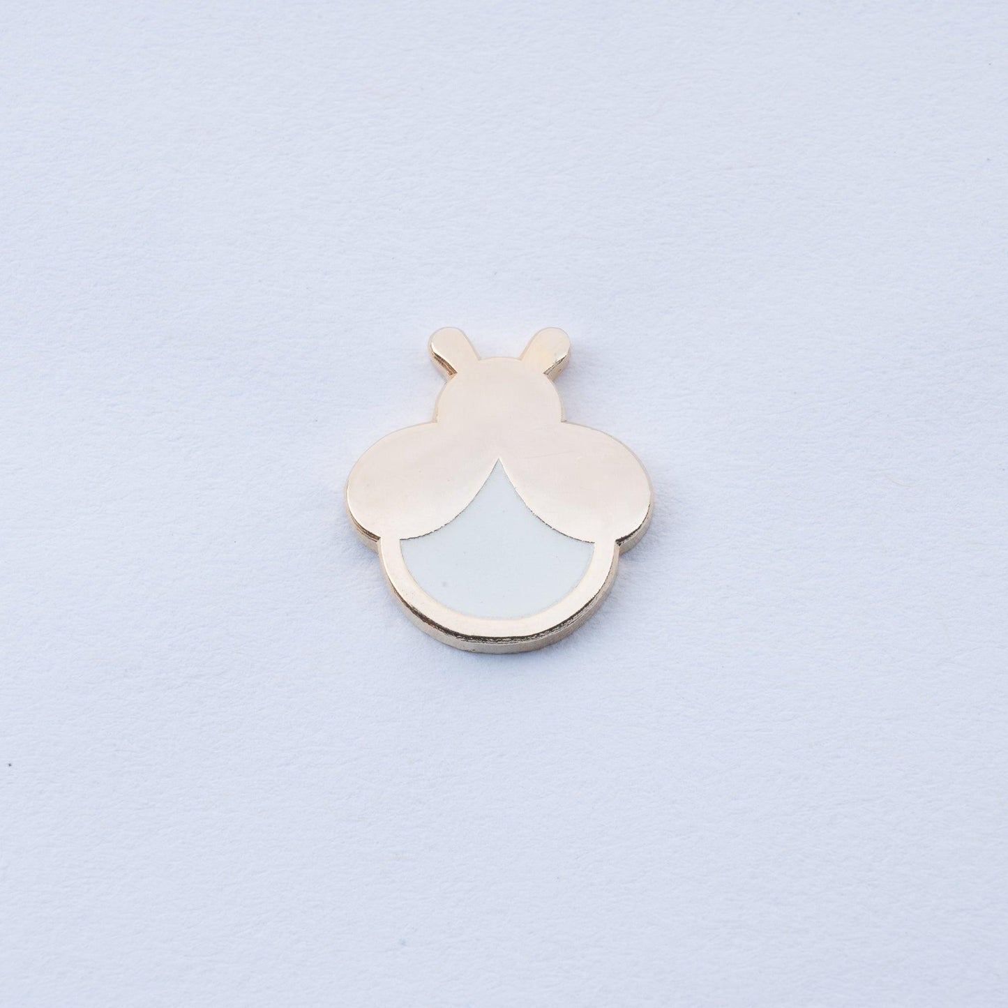 gold plated firefly enamel pin with white body that glows in the dark