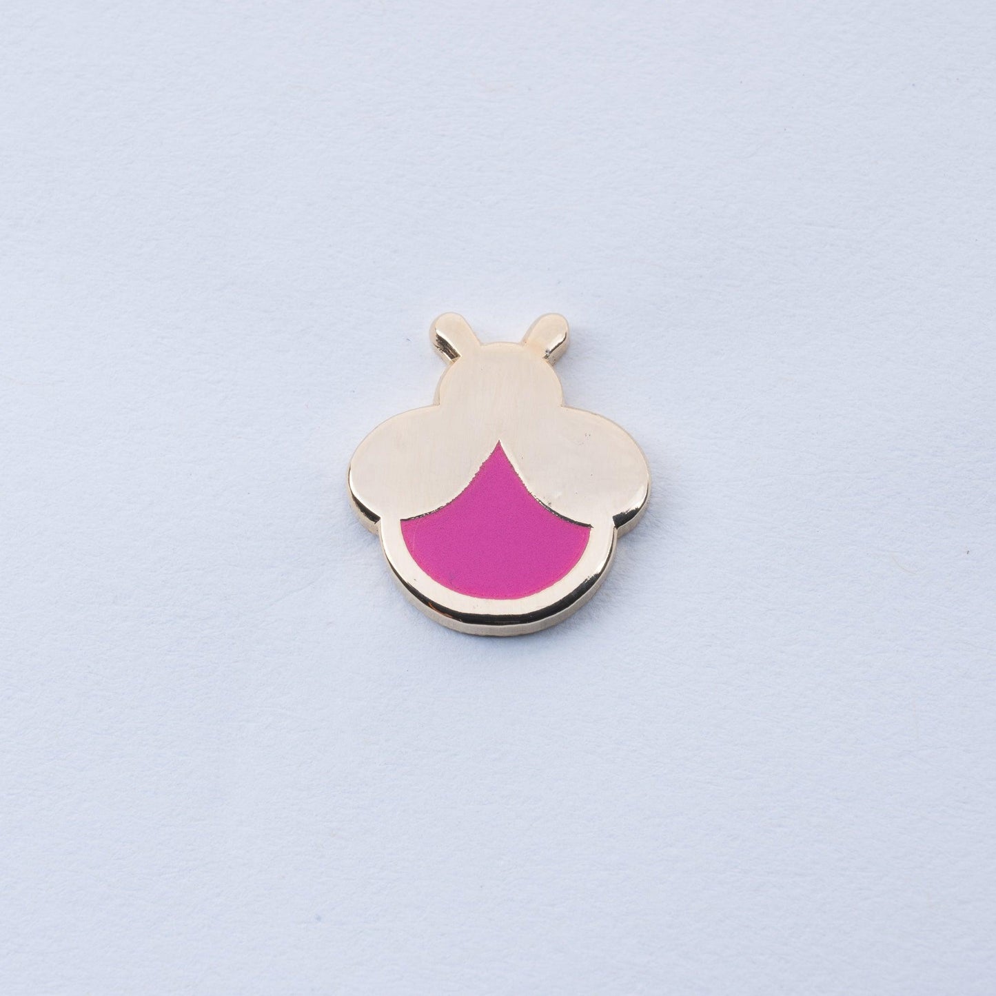 gold plated firefly enamel pin with magenta body that glows in the dark