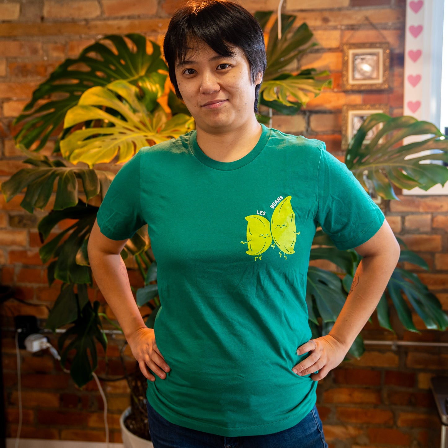 a green shirt with cute cartoon edamame characters holding hands on the left breast. white text above them saying "les beans"