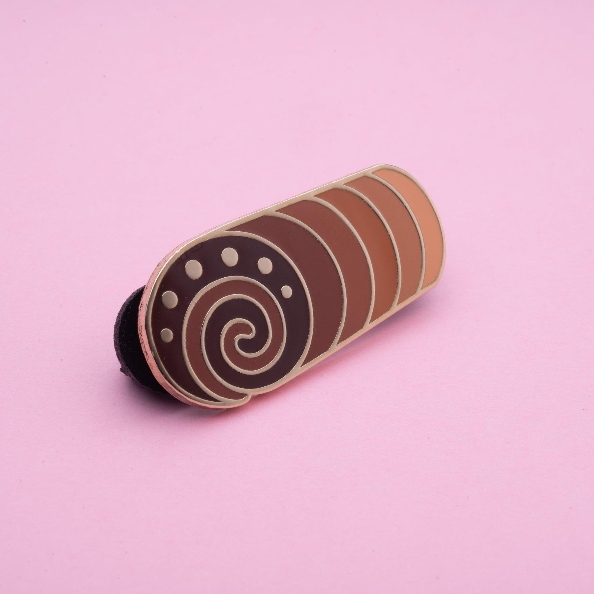 chocolate cake swirl enamel pin where each section is a different shade of chocolate and at the front is the darkest chocolate and a brown chocolate cream swirl