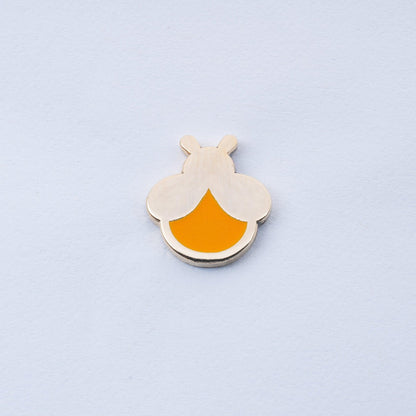 gold plated firefly enamel pin with orange body that glows in the dark